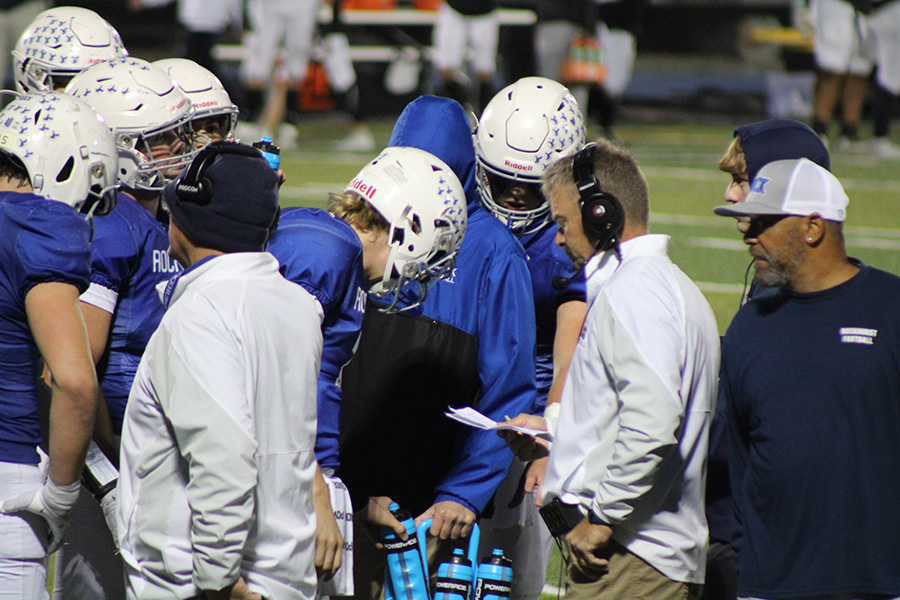 Offensive players huddle up around head coach Kelly Donohoe during the first half of Rockhursts game against SLUH on Oct. 13, 2023. The Hawklets would go on to win 40-22.