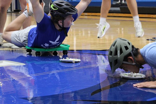 Senior Campbell Luzar raises his hands to signify he finished the "Hungry Hungry Hippos"-style game during the first pep assembly on Aug. 29, 2025.  Representatives from each class took part in the game that involved a student on a scooter eating powdered sugar donuts off a plate without using his hands. Luzar was the first to complete the task, besting junior Oliver Arnold (right) in the process.